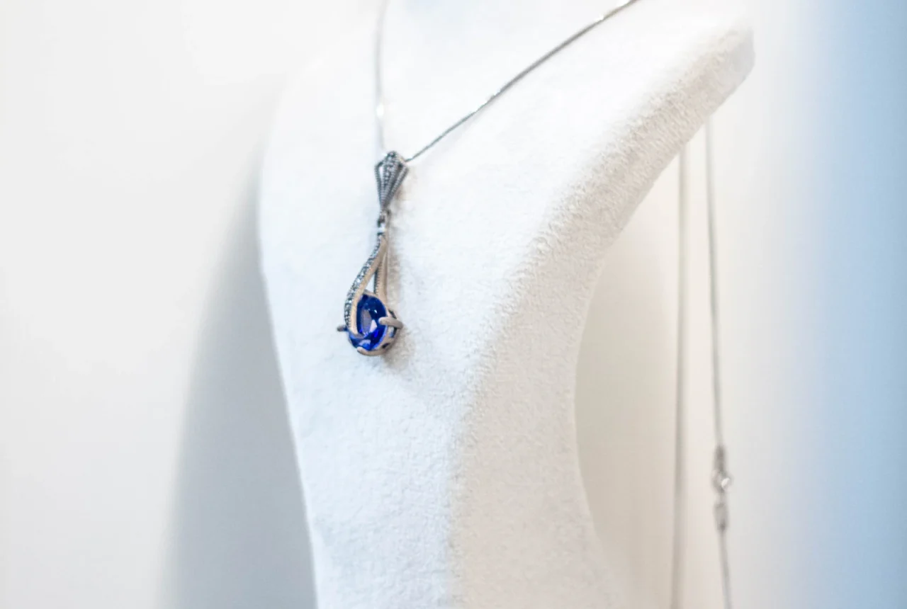 Blue gemstone pendant necklace and matching earrings displayed on white jewelry stands