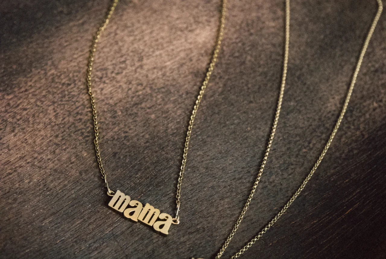 Gold Mama name necklace and flower pendant necklace on a dark wooden surface