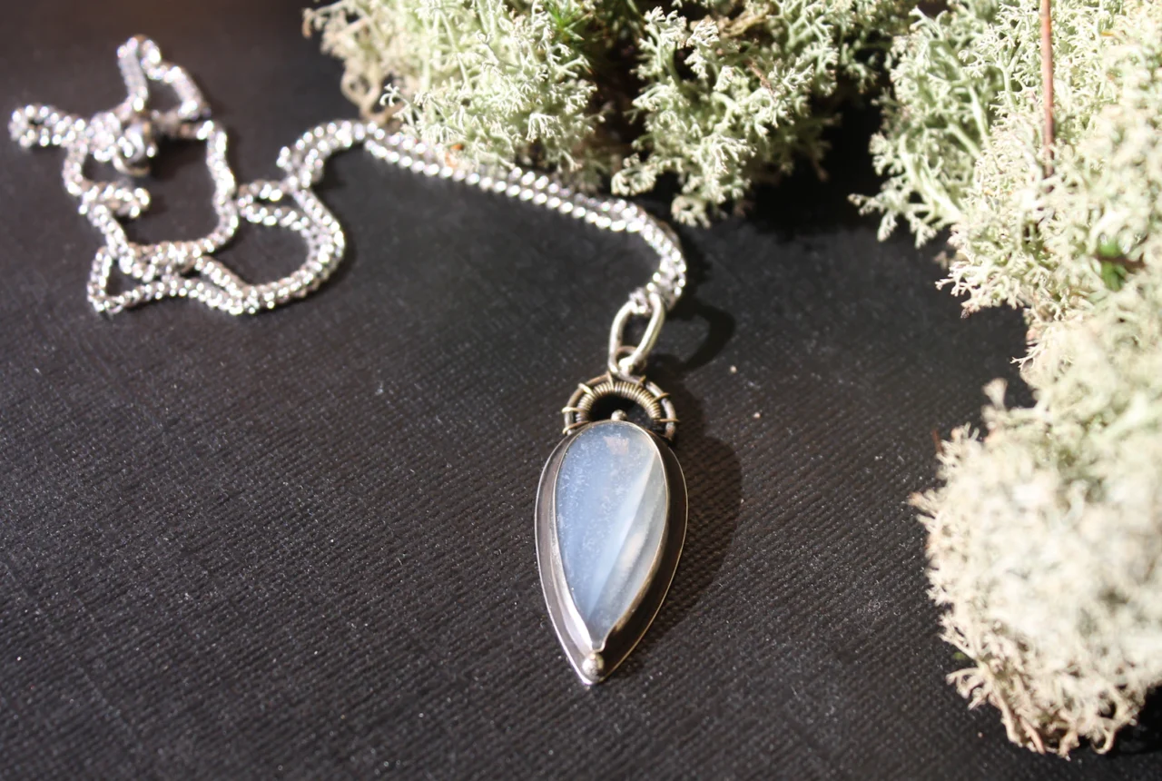 Silver necklace with a teardrop gemstone pendant on a dark surface